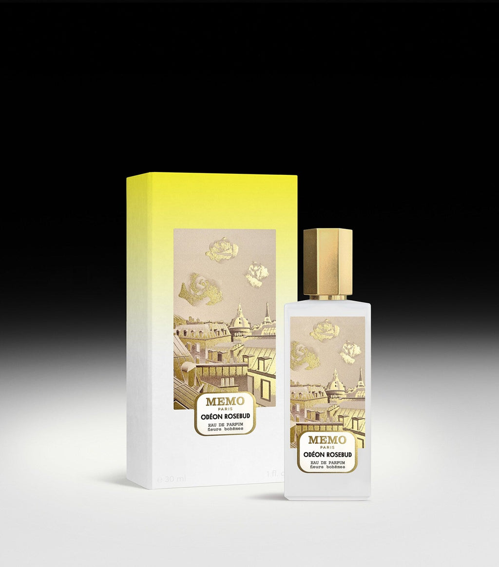 Frosted white rectangular perfume bottle with gold-toned cap and label showing Parisian rooftops and rosebuds. Matching yello