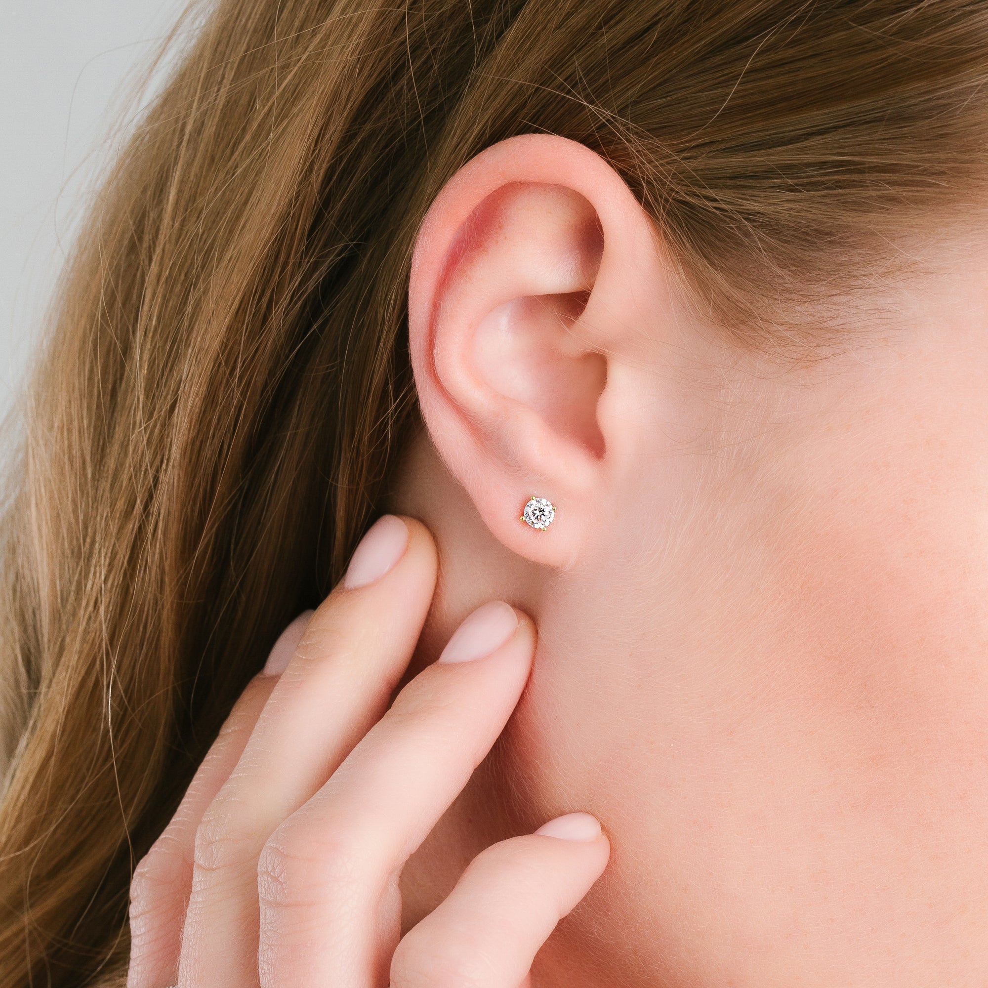 A single round clear stud earring with a gold-toned four-prong setting.