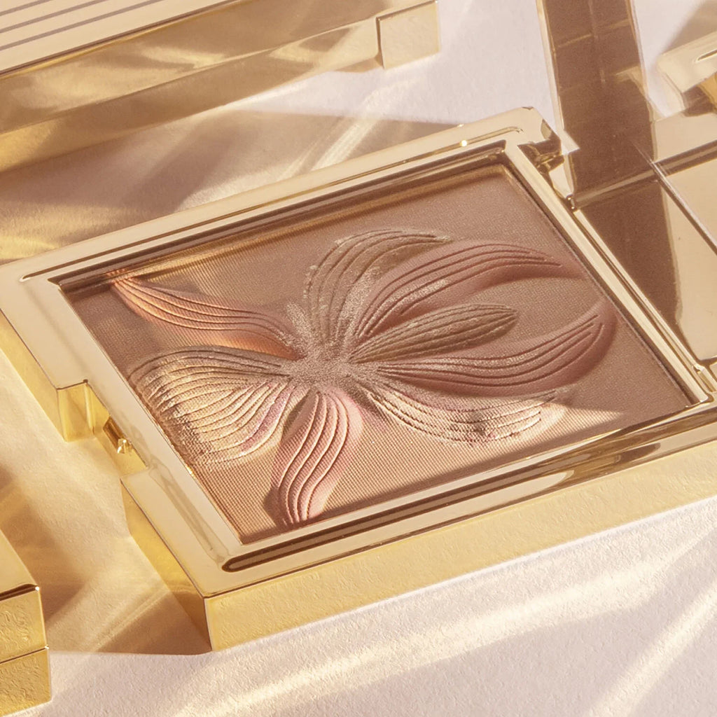 Gold-toned rectangular compact with bronze powder featuring a raised orchid design in varying shades of bronze and pinkish-br