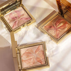 Square gold-toned compact with bronze pressed powder featuring a raised orchid design with pink and gold-toned glitter accent