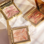 Square gold-toned compact with bronze pressed powder featuring a raised orchid design with pink and gold-toned glitter accent