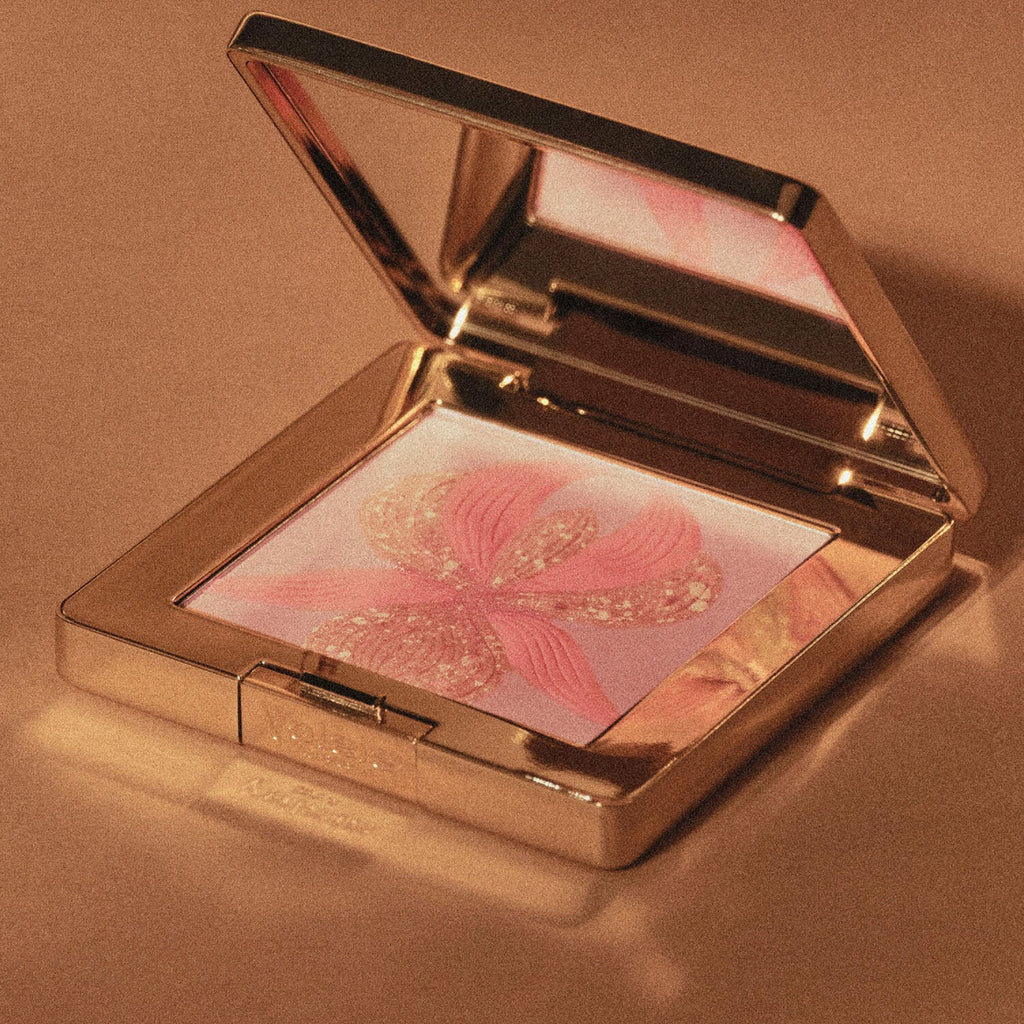 Gold-toned compact, open to reveal a mirror and pressed powder. Powder has a peachy-pink flower with glittery gold-toned deta