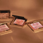 Gold-toned square compact with an open lid, revealing pressed powder with an embossed pink, peach, and gold-toned orchid desi