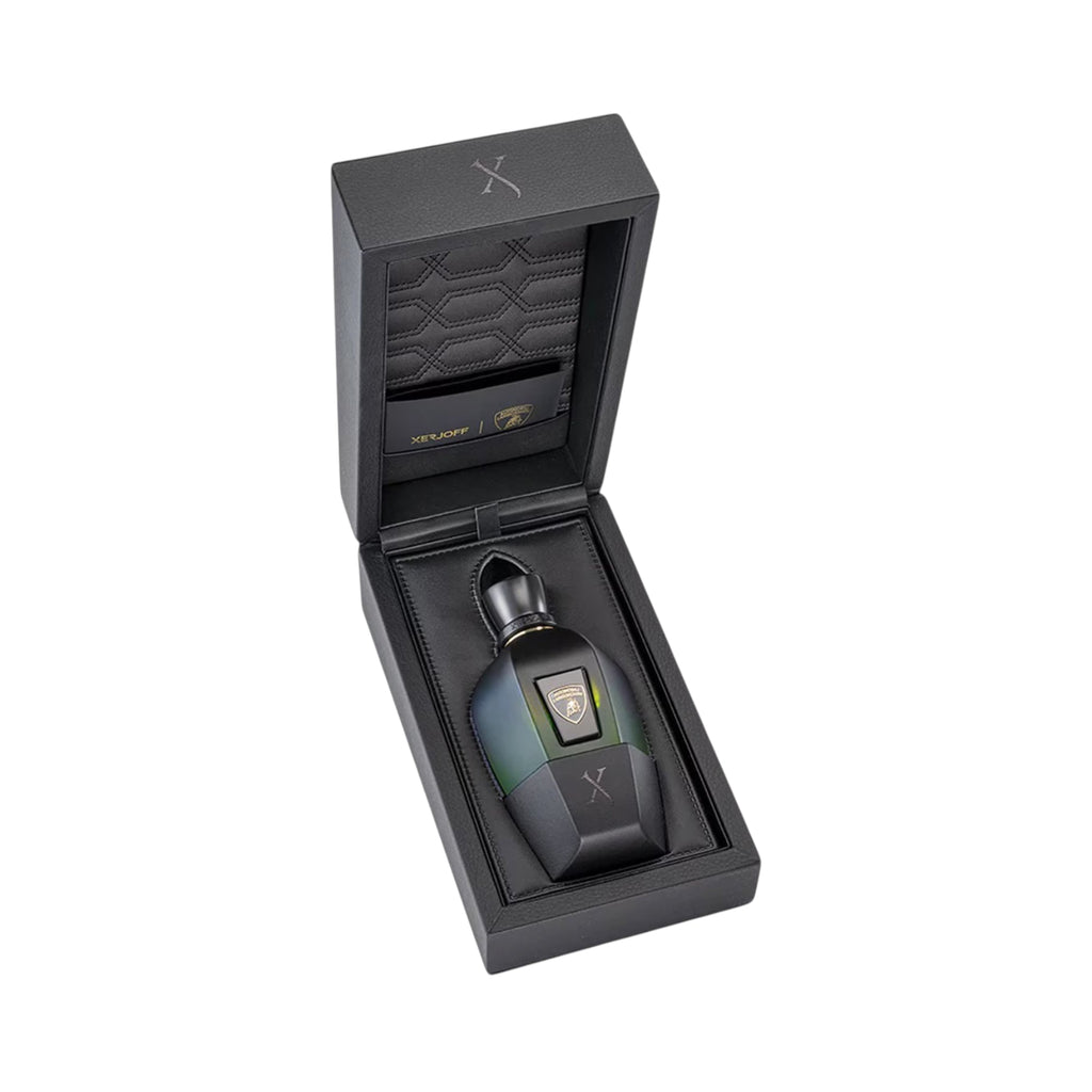 Black textured box with a dark multi-faceted perfume bottle. Bottle has a blue-green to black gradient, gold-toned cap, and L