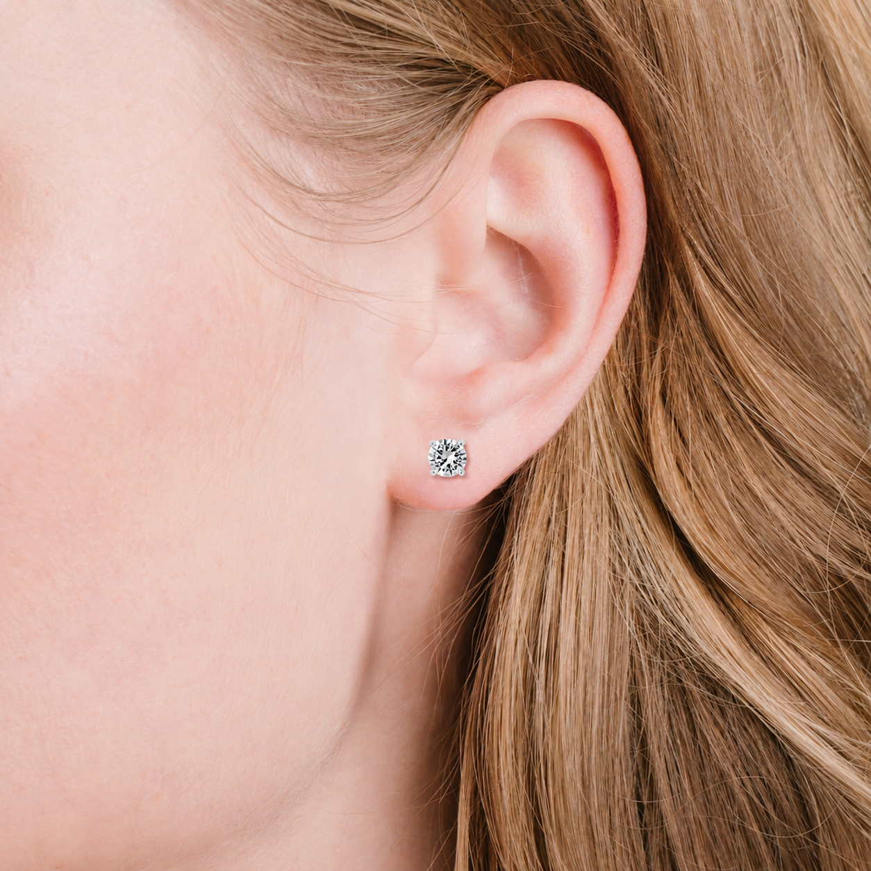 A single round, clear, faceted stud earring in a silver-toned four-prong setting.