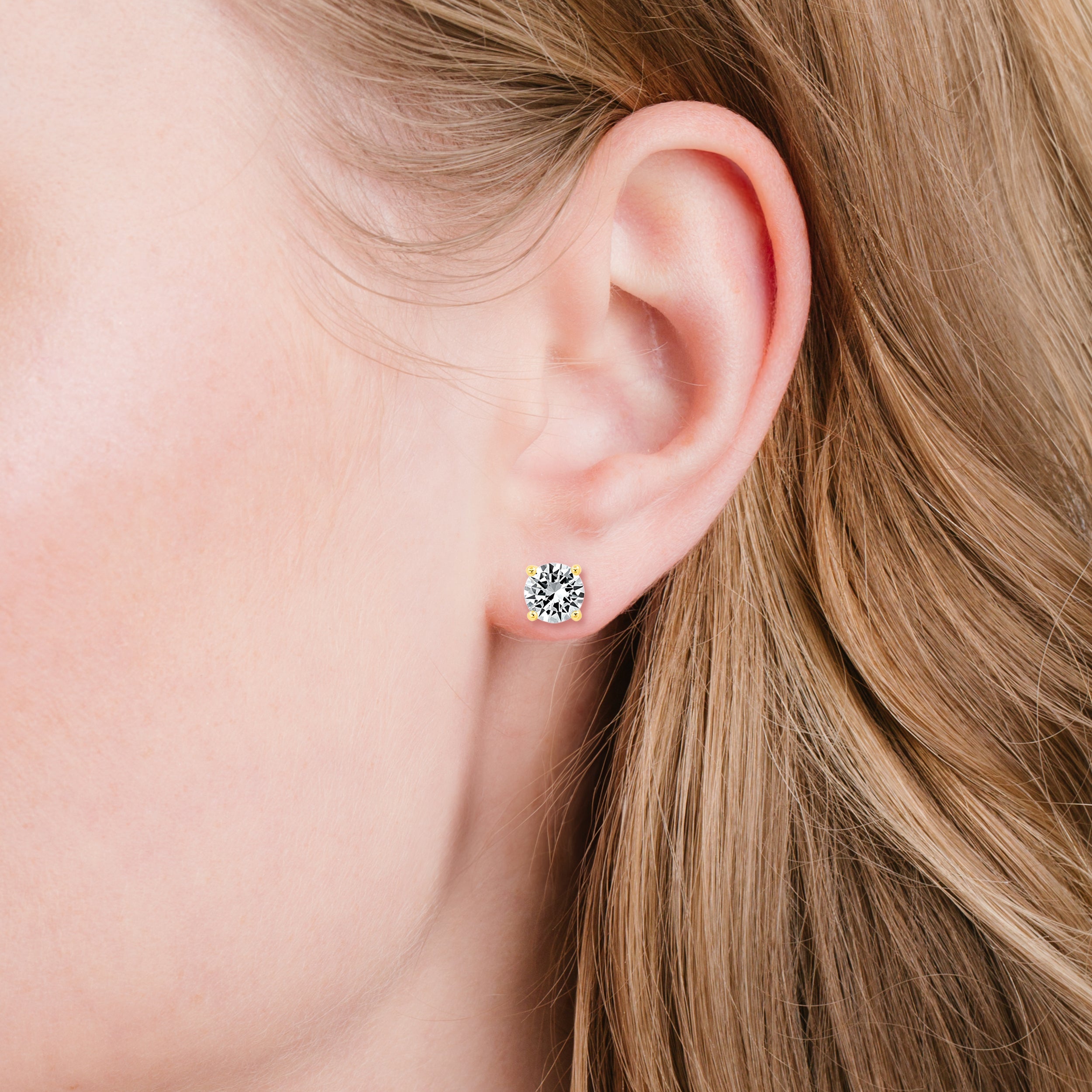 Single stud earring with a round, clear, faceted stone in a four-prong gold-toned setting.