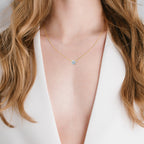 A gold-toned necklace with a delicate chain and a round, clear stone pendant held by six silver-toned prongs.