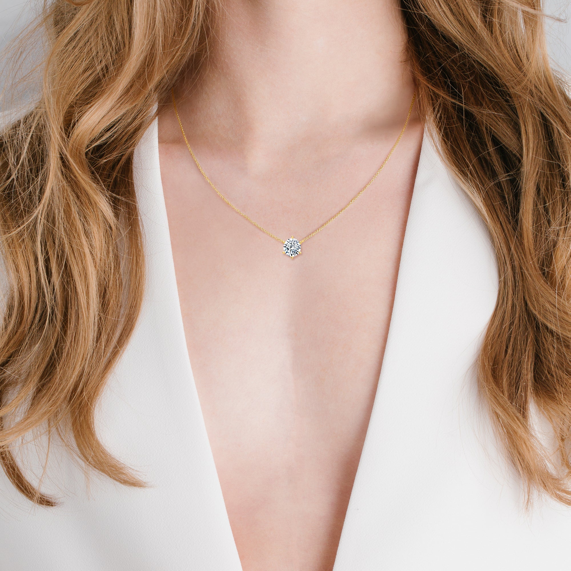 A gold-toned necklace with a delicate chain and a round, clear stone pendant held by six silver-toned prongs.