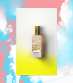 Frosted glass perfume bottle with light pink liquid, gold-toned hexagonal cap. Label has gold-toned rosebuds and a cityscape.