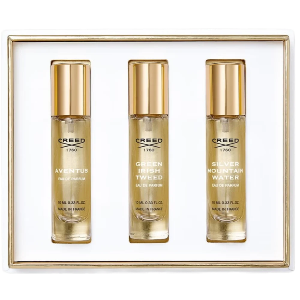 White gift set box containing three clear glass fragrance bottles with gold-toned caps and labels for Creed Aventus, Green Ir