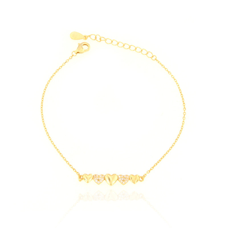 Gold-toned delicate chain bracelet with five heart charms, two of which are encrusted with clear stones, and a lobster clasp.