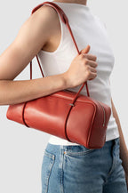  BY FAR Kimberly shoulder bag in blood red nappa leather featuring a long rectangular body and two thin tubular straps against a light grey background.