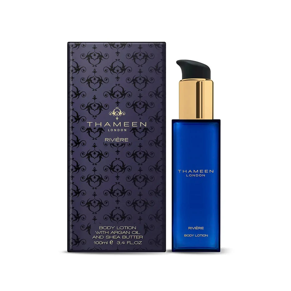 Dark blue rectangular body lotion bottle with gold-toned pump and black cap, next to a dark purple box with black scrollwork.