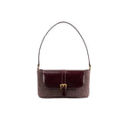 Front view of the BY FAR Miranda baguette bag featuring a purple grape-colored woven raffia body, a smooth dark leather front flap, and a gold buckle against a grey background.