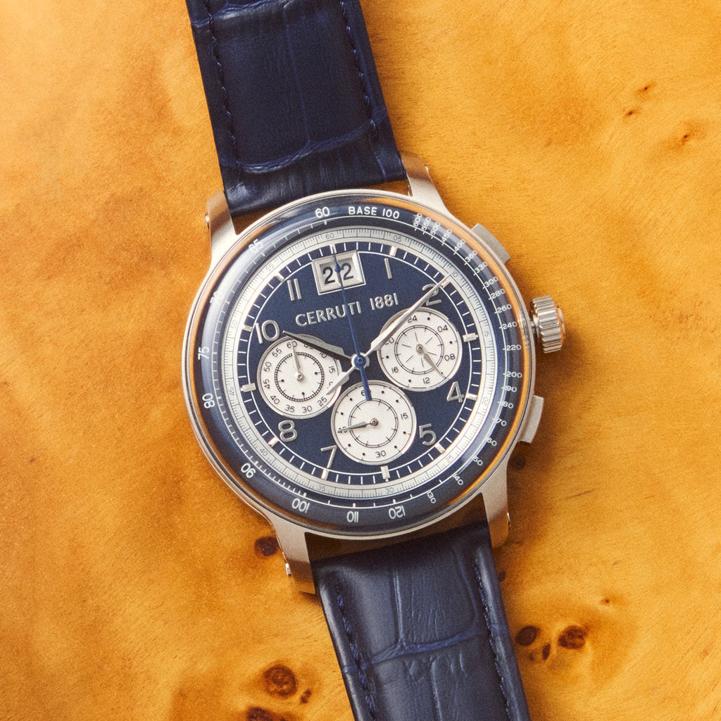 Silver-toned watch with a dark blue dial, three white sub-dials, and a date window. Features a dark blue crocodile-embossed l