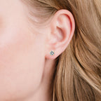 A single round, clear, faceted stud earring with a gold-toned four-prong setting.