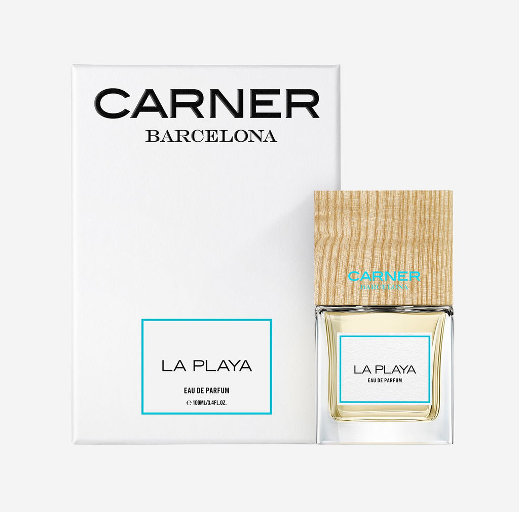 Carner Barcelona La Playa perfume bottle featuring a heavy, clear glass base, minimalist white label with black text, and a signature large, dark square wooden cap.