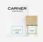 Carner Barcelona La Playa perfume bottle featuring a heavy, clear glass base, minimalist white label with black text, and a signature large, dark square wooden cap.