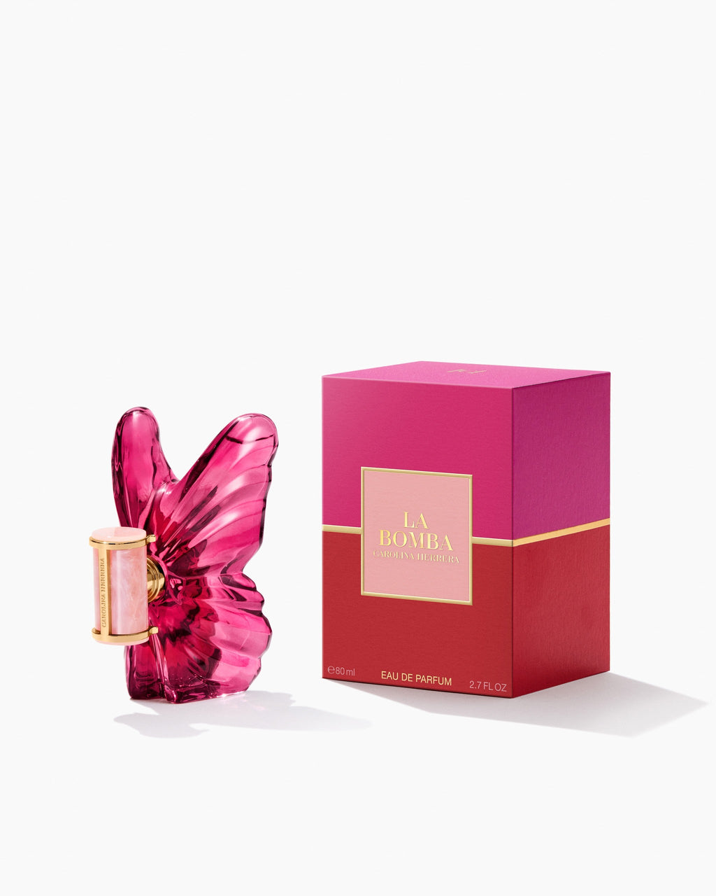 The Carolina Herrera La Bomba 80ml fragrance bottle standing next to its square display box, which features a bold color-blocked design in bright pink and deep red with gold trim and "LA BOMBA" printed on a central pink label.