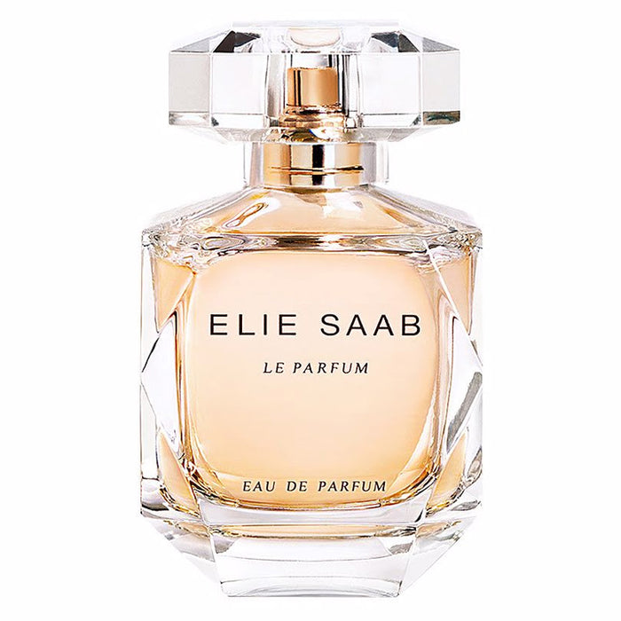 Front view of the Elie Saab Le Parfum Eau de Parfum 90ml bottle against a plain white background. The bottle is crafted from clear, heavy faceted glass resembling a cut gemstone, revealing the peach-colored liquid inside. It features a transparent, geometric crystal-like cap with a gold dispenser underneath, and 'ELIE SAAB LE PARFUM EAU DE PARFUM' printed in black lettering across the front.