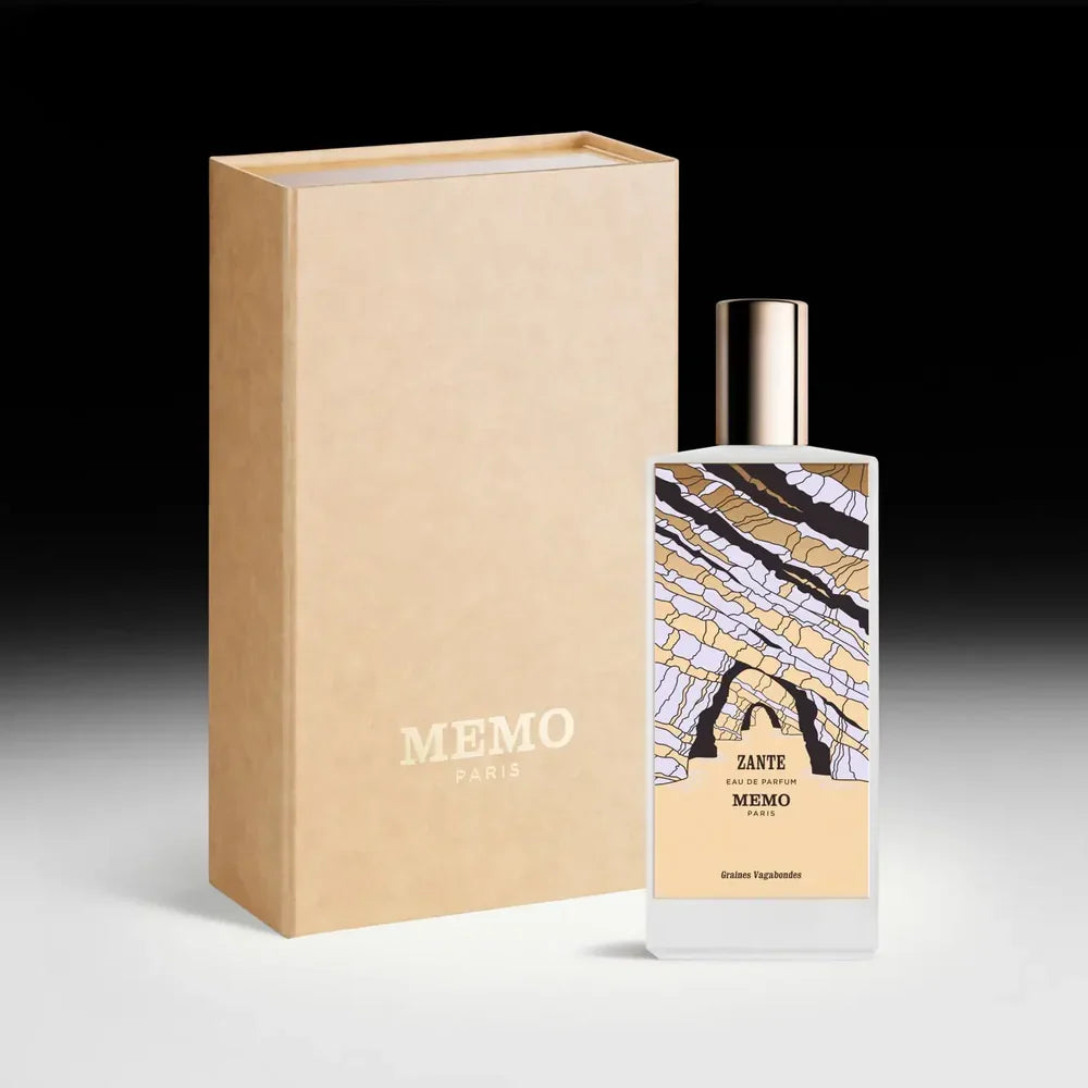 : A white bottle of Memo Paris Zante Eau de Parfum standing next to its tan textured presentation box. The bottle features a colorful, abstract illustration of coastal rock formations.