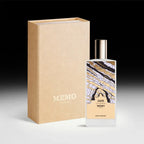 : A white bottle of Memo Paris Zante Eau de Parfum standing next to its tan textured presentation box. The bottle features a colorful, abstract illustration of coastal rock formations.