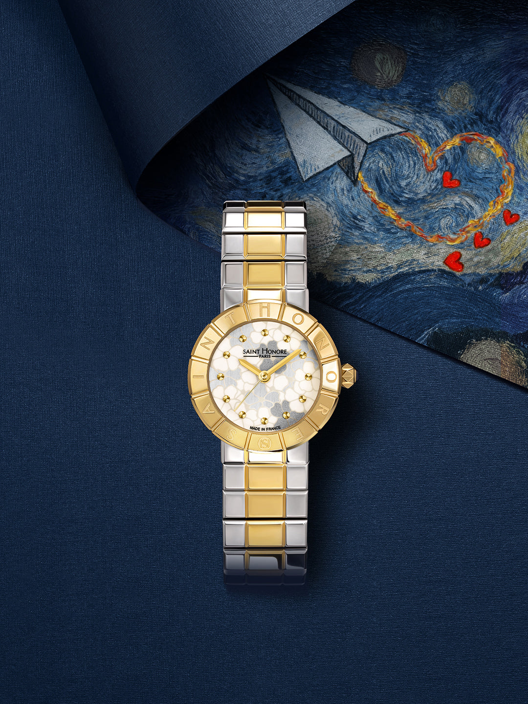 Two-toned gold-toned and silver-toned watch with a round gold-toned case, white floral pattern dial, and metal link bracelet.