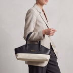 Structured black leather and off-white canvas handbag with a curved top, two handles, and a gold-toned logo.