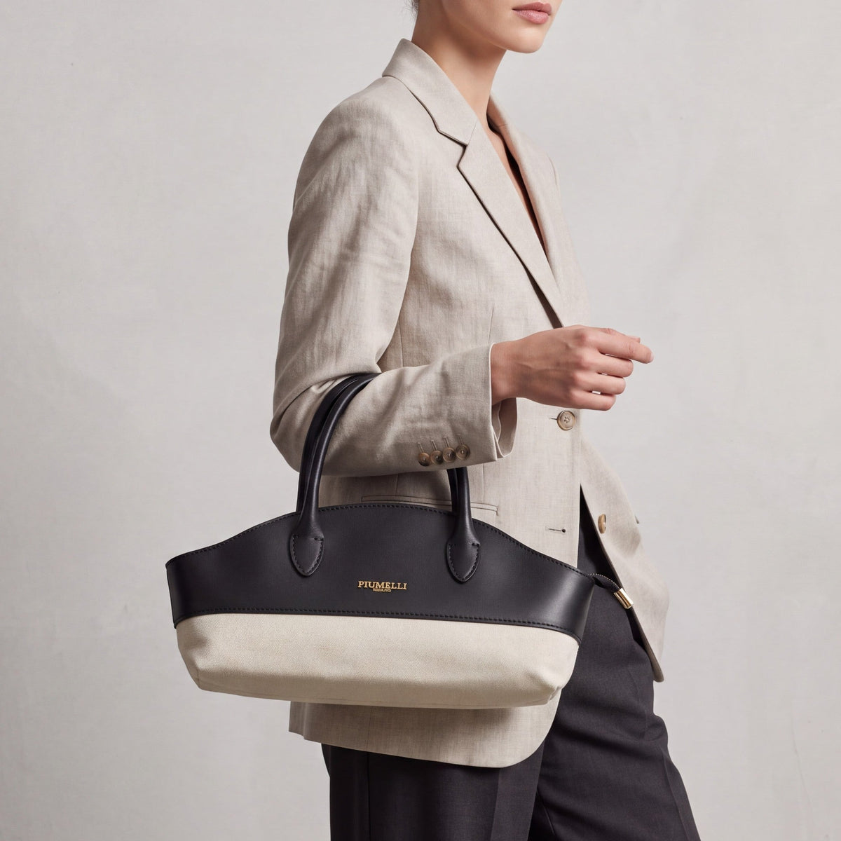 Structured black leather and off-white canvas handbag with a curved top, two handles, and a gold-toned logo.