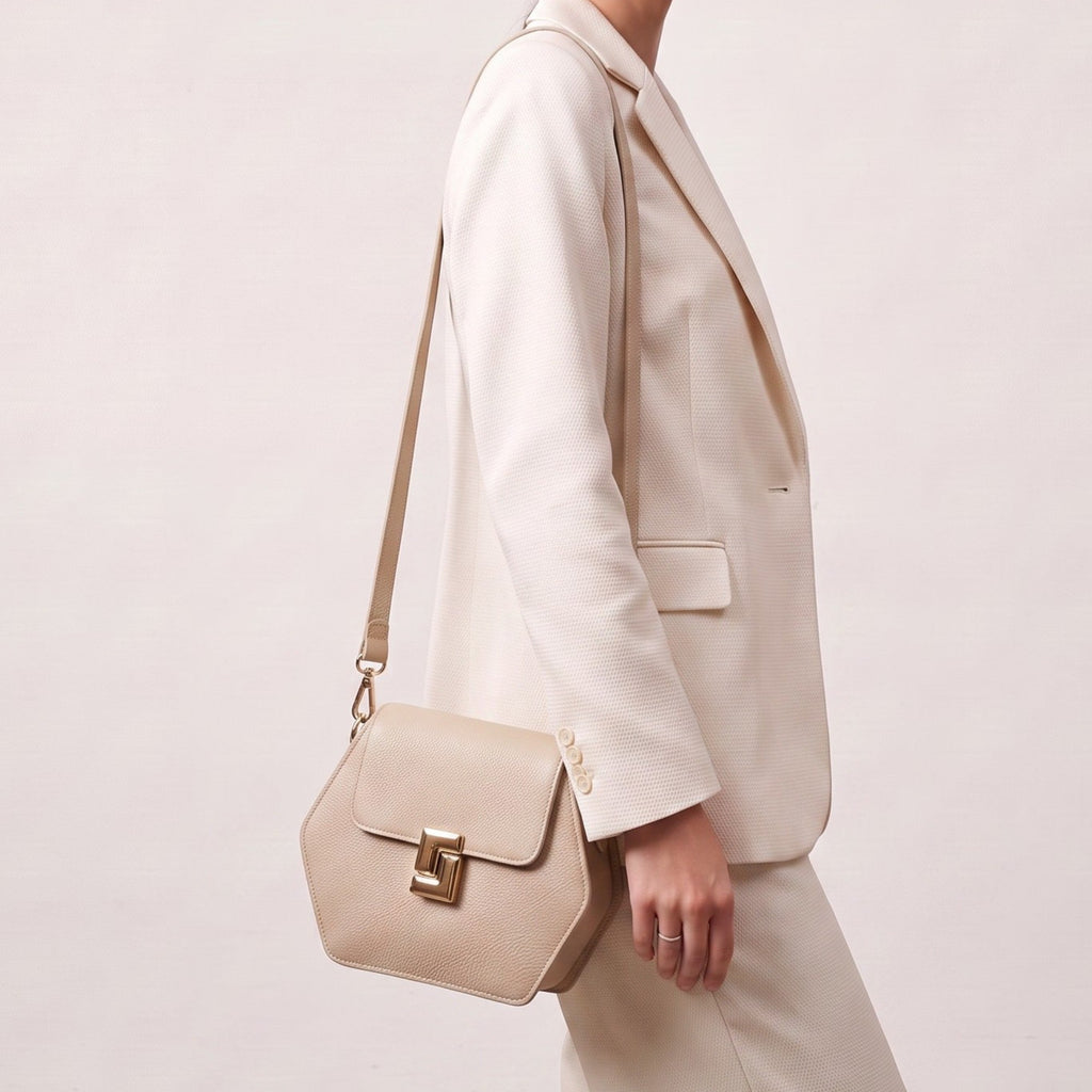 Ivory pebbled leather hexagonal bag with a front flap, unique gold-toned geometric clasp, and a thin shoulder strap.