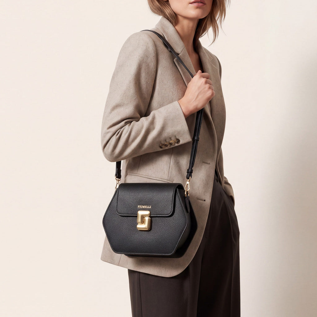 Black pebbled leather hexagonal crossbody bag with a flap closure, gold-toned hardware, 'FIUMELLI' branding, and a twist-lock