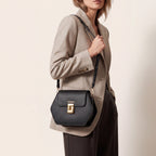 Black pebbled leather hexagonal crossbody bag with a flap closure, gold-toned hardware, 'FIUMELLI' branding, and a twist-lock
