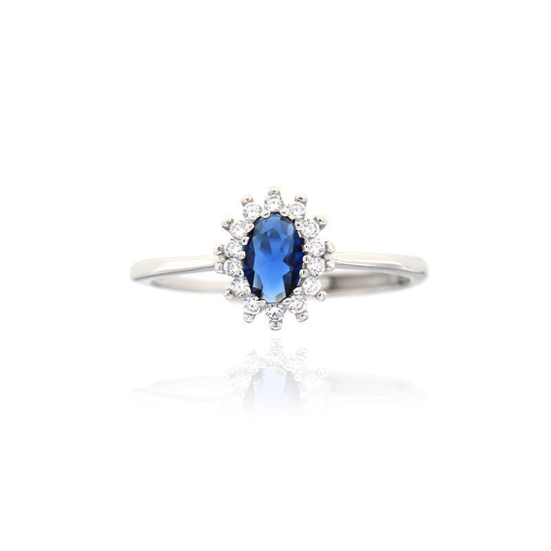 Silver-toned ring with a central oval dark blue stone surrounded by a halo of small clear stones on a thin band.