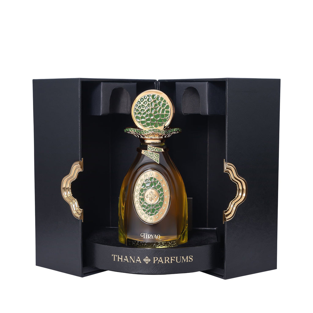 Amber perfume bottle with gold-toned cap and green mosaic details. In open black box with gold-toned wavy handles.