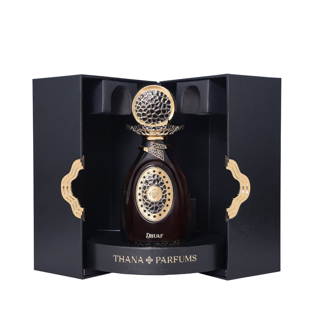 Dark amber perfume bottle with a gold-toned ornate cap and front design, displayed in a black textured box with gold-toned wa