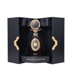 Dark amber perfume bottle with a gold-toned ornate cap and front design, displayed in a black textured box with gold-toned wa