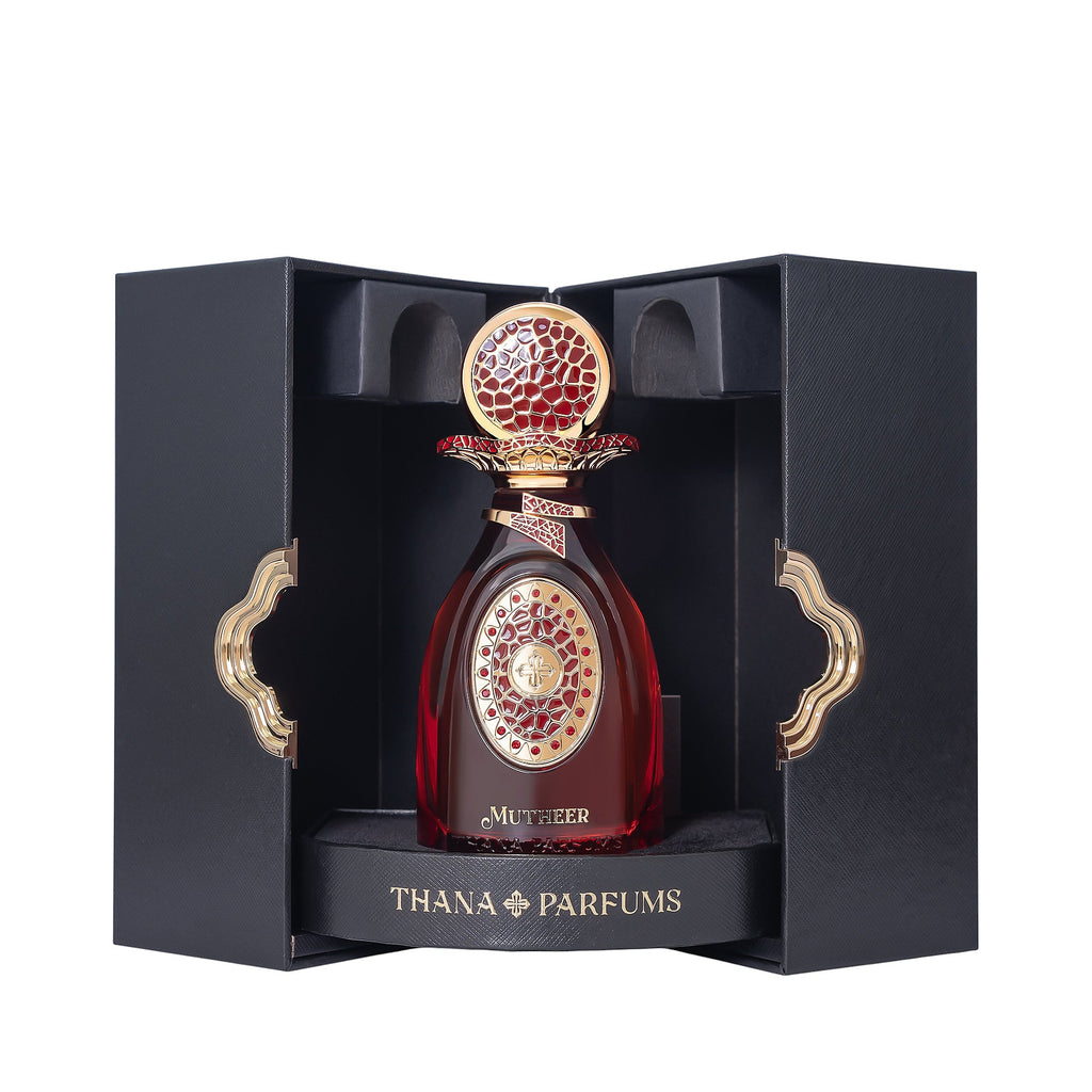 Dark red perfume bottle with an ornate gold-toned cap and label, presented in a black textured box with gold-toned clasps.
