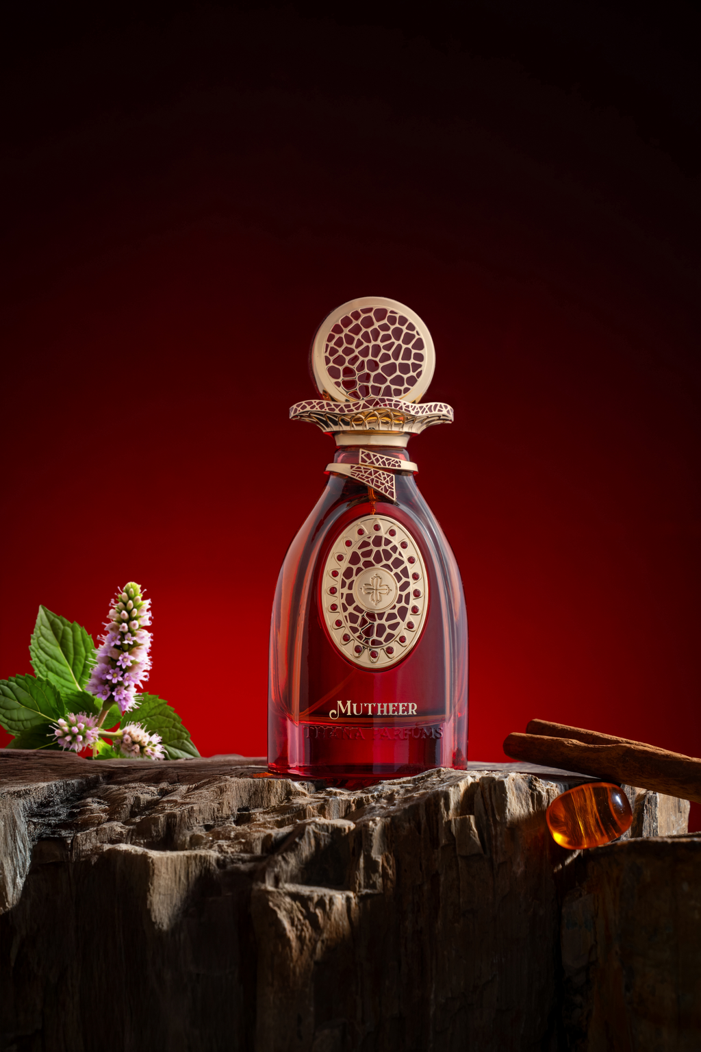 Deep red perfume in a clear glass bottle with a gold-toned cap and neck, both featuring intricate cut-out patterns. Gold-tone