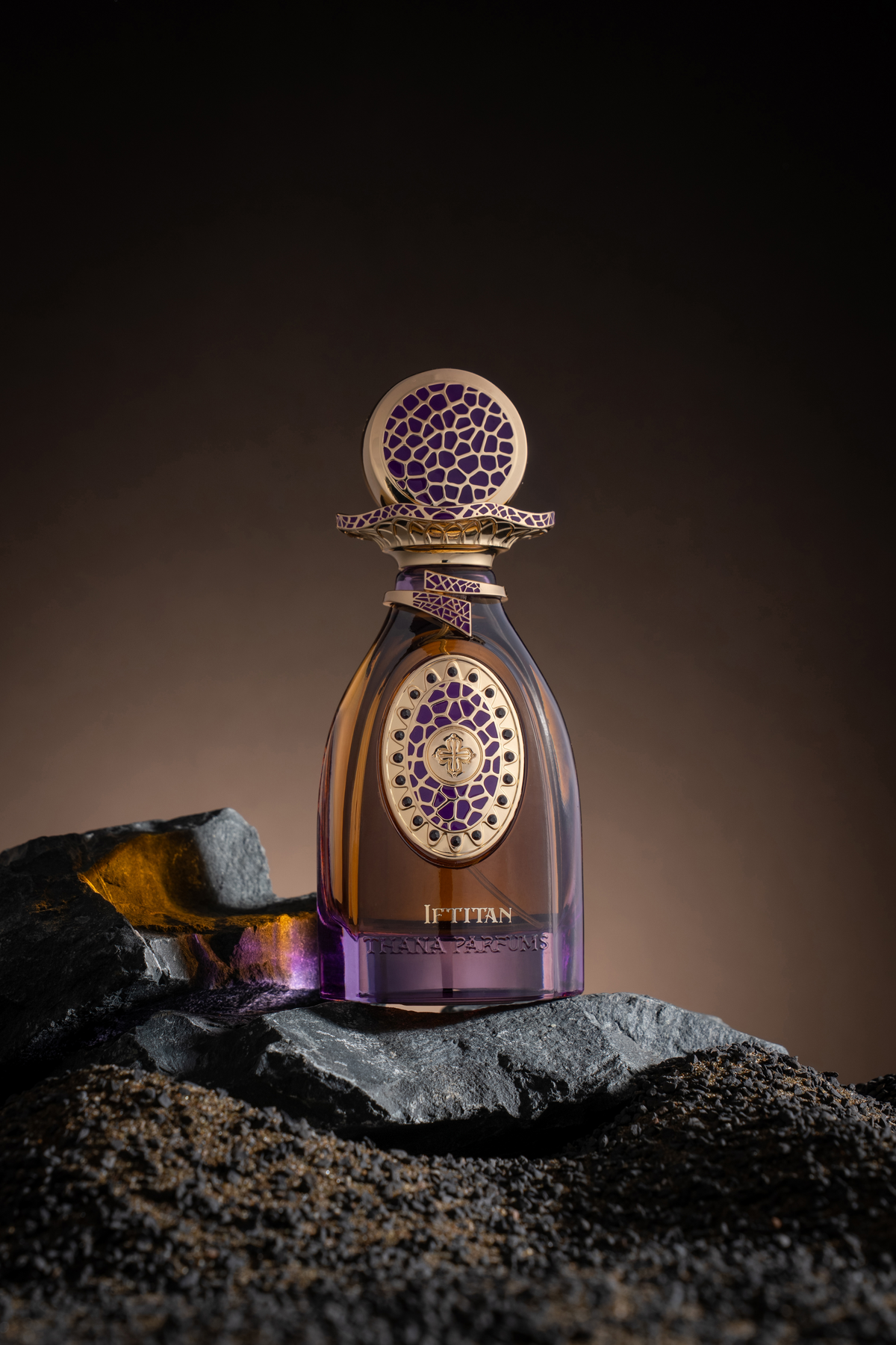 Amber and purple glass perfume bottle with a gold-toned cap. Cap and bottle's oval label feature purple mosaic patterns with