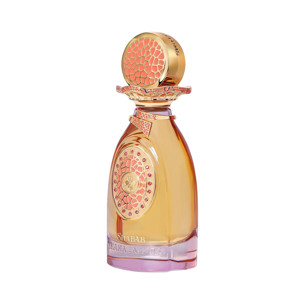 Amber perfume bottle with pink-tinted base, gold-toned cap with coral mosaic top, and a gold-toned emblem with pink gems.