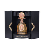 Black box with gold-toned trim holds an amber perfume bottle. It has a gold-toned cap with coral-pink texture and an ornate g