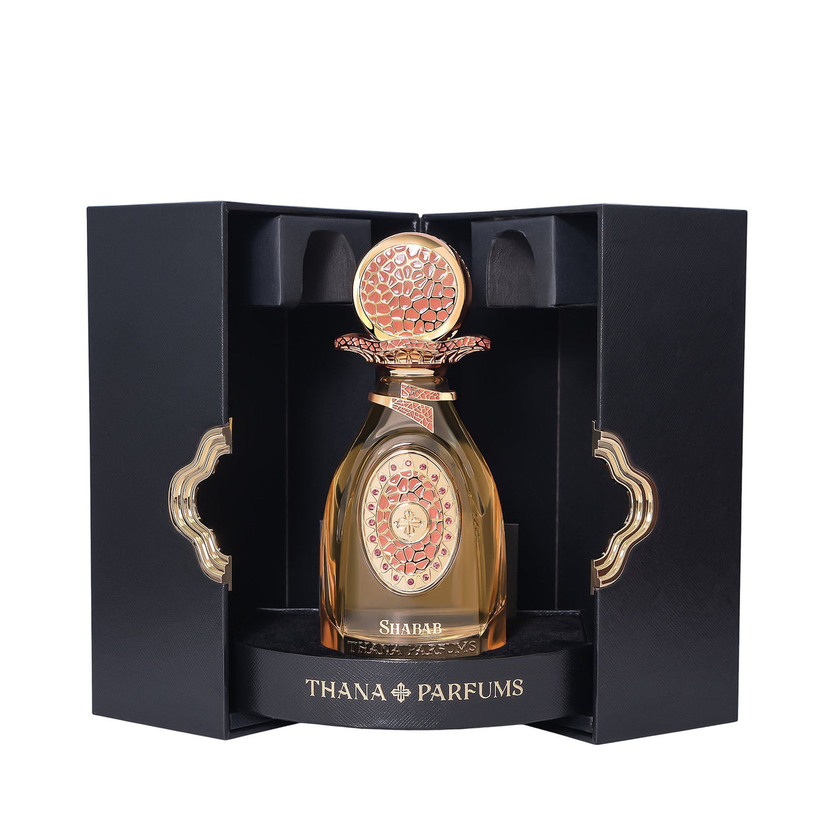 Black box with gold-toned trim holds an amber perfume bottle. It has a gold-toned cap with coral-pink texture and an ornate g