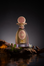 Clear glass perfume bottle with gold-toned liquid. Gold-toned cap, collar, and front emblem with pink mosaic, pink gems, and