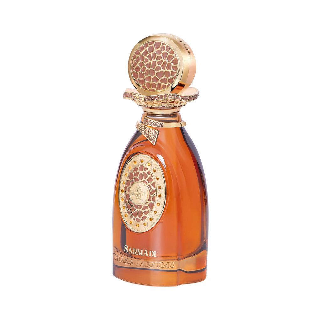 Amber glass perfume bottle with a gold-toned ornate cap featuring a textured pattern. A gold-toned medallion with amber studs