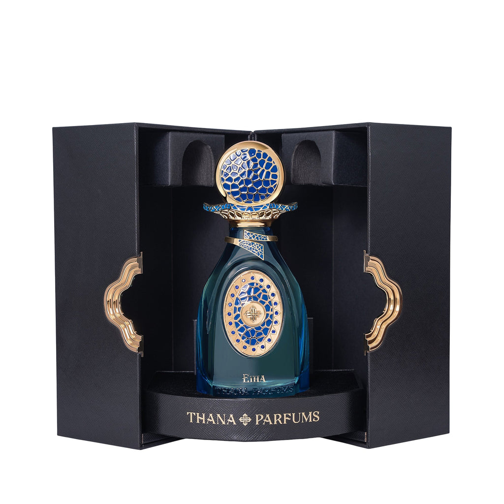 Teal glass perfume bottle with gold-toned and blue mosaic patterns, topped with a matching cap, presented in an open black bo