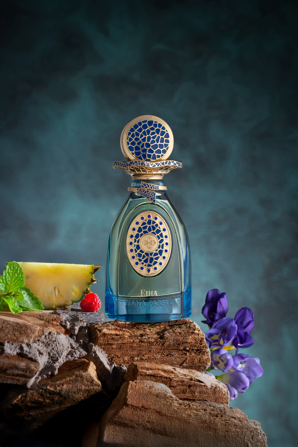 Blue-tinted glass perfume bottle with light blue liquid. Features a gold-toned cap and label, both with intricate blue mosaic