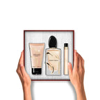 A Giorgio Armani Si gift set: a peach body lotion tube, a clear perfume bottle with gold-toned wavy accents, and a peach Si t