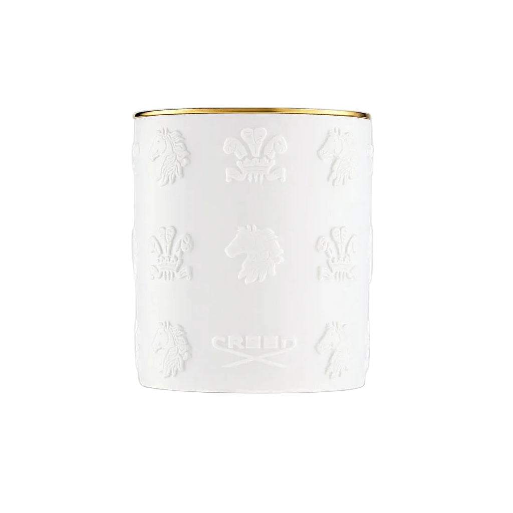 White cylindrical candle with a gold-toned rim and embossed patterns of horse heads and crests, with "CREED" text.