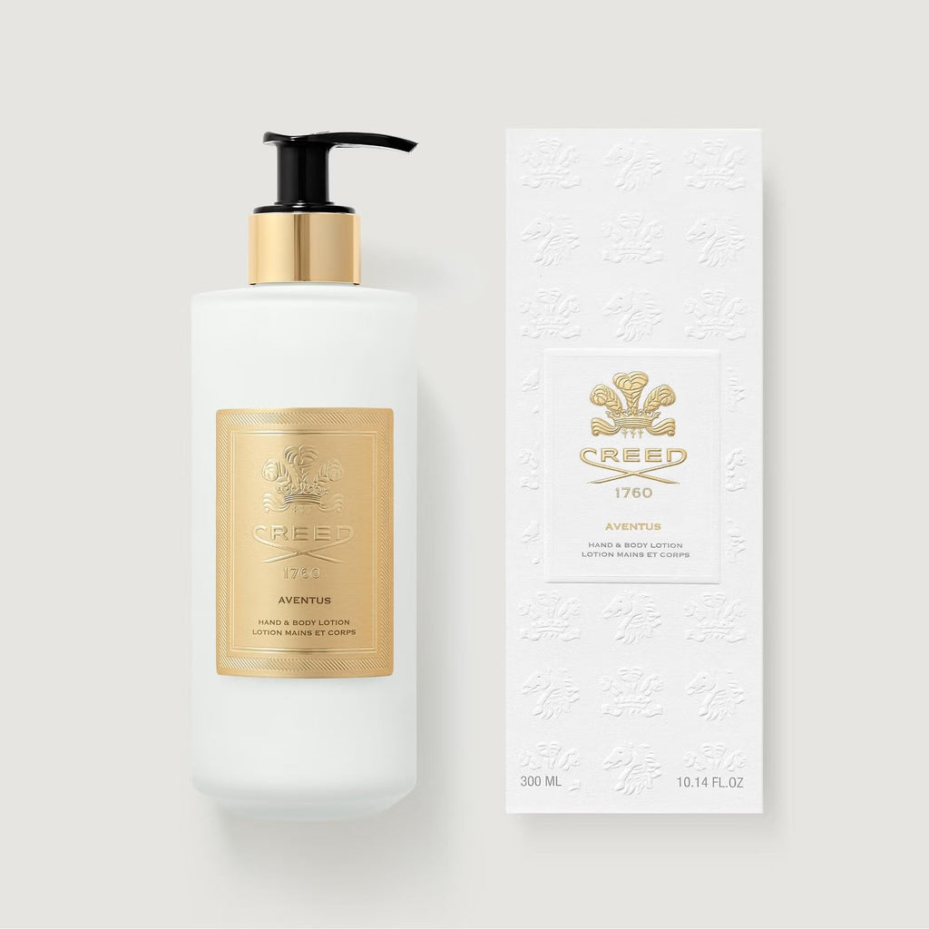 White lotion bottle with black pump and gold-toned collar, next to a white embossed box, both featuring gold-toned Creed labe