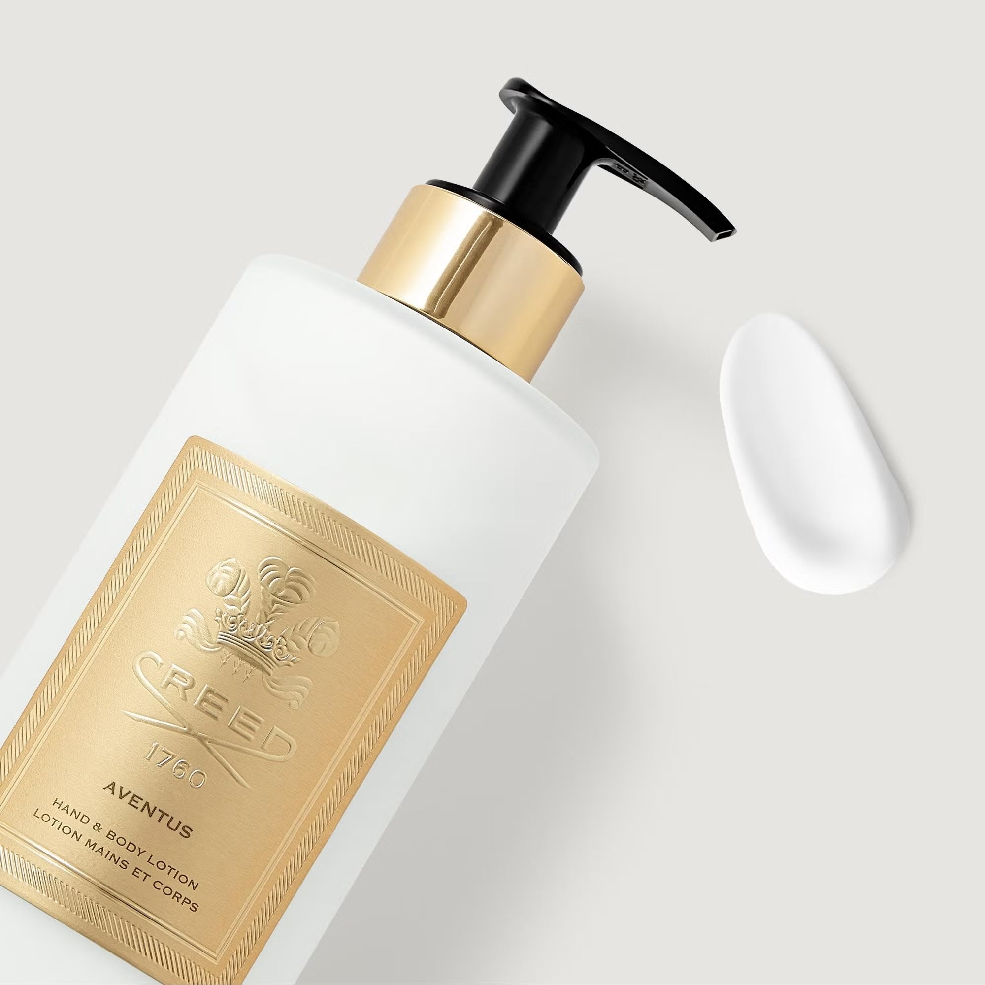 White opaque bottle with a black pump dispenser and gold-toned collar. A gold-toned label with a crest and "CREED AVENTUS" te